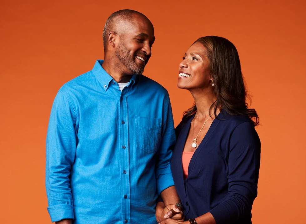 A middle aged couple standing, holding hands, and smiling at each other