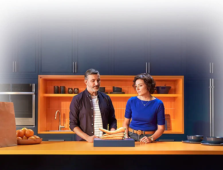 A couple standing in an orange kitchen looking at a plate of bent carrots