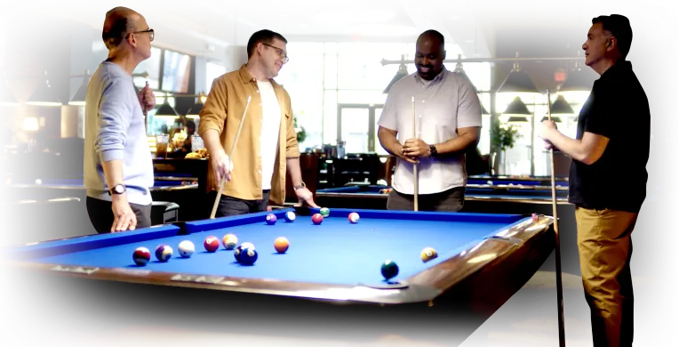 Four actual patients with Peyronie’s disease standing together around a pool table discussing their condition and possible treatment with XIAFLEX