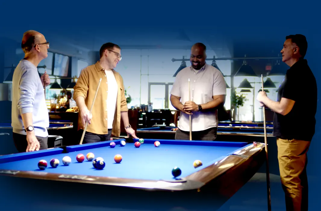 Four actual patients with Peyronie’s disease standing together around a pool table discussing their condition and possible treatment with XIAFLEX