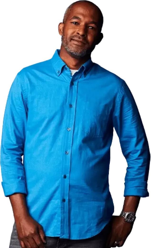 A middle aged man in a blue shirt staring confidently at the camera with his hands in his pockets